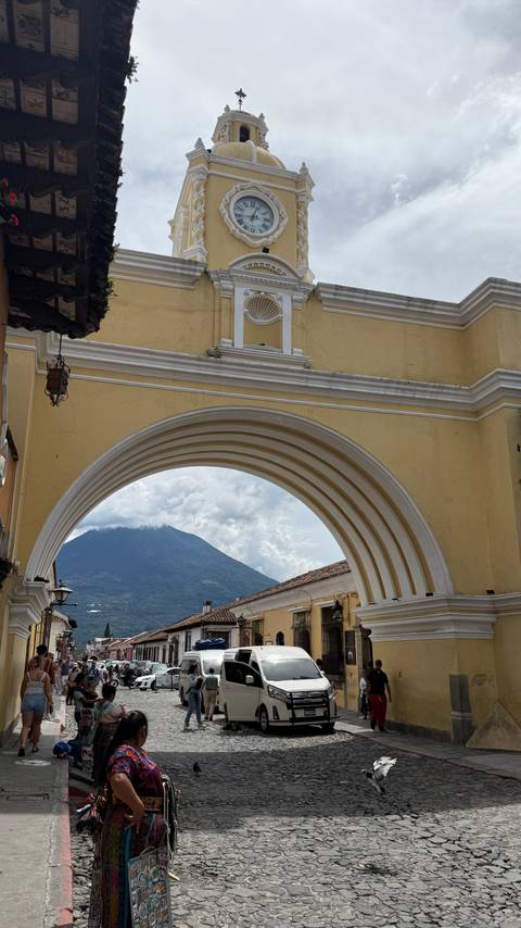 Iconic yellow arch frames a distant volcano under partly cloudy skies in a colonial city.