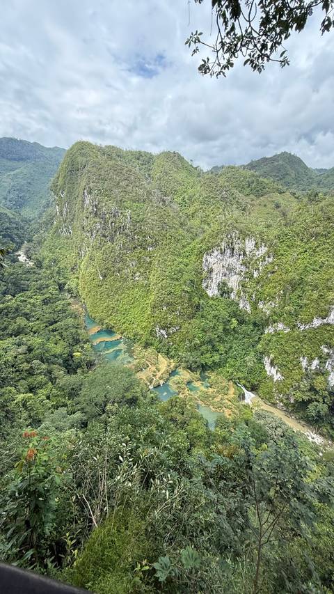 Aerial viewpoint of turquoise river pools and dense jungle cliffs in a limestone valley.
