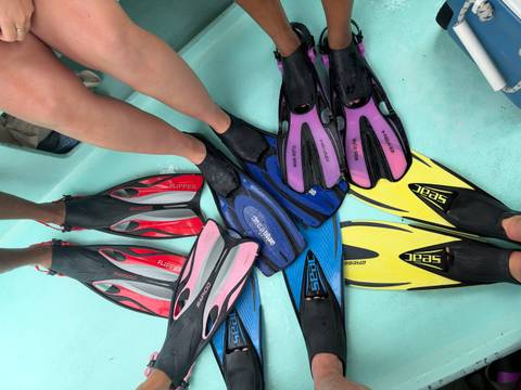 Collection of colorful snorkel fins and bare legs arranged in a circle on a boat deck.