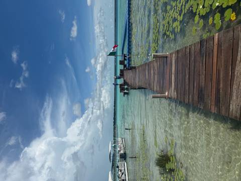Wooden jetty stretches over crystal-clear turquoise lagoon toward open water and sky.