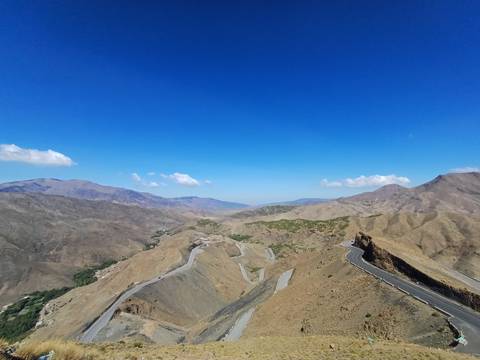 Panoramic view of winding mountain highway and barren high-atlas ridges beneath blue sky.