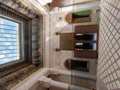 Intricately tiled interior courtyard with carved cedar ceilings and skylight in a Moroccan madrasa.