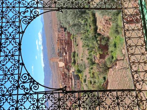 Rustic village and mosque tower framed by ornate wrought-iron window overlooking green valley.