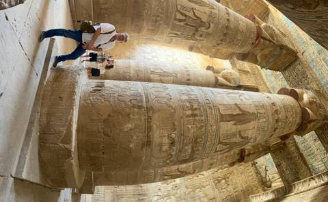Towering decorated columns filled with vibrant hieroglyphs rise above visitors in ancient temple.