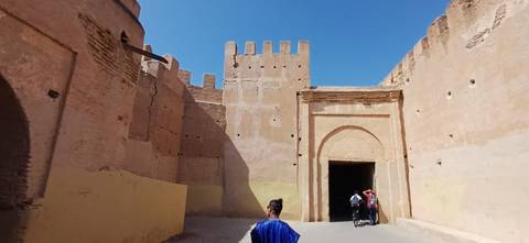 Adobe fortress walls and arched gateway under a bright blue sky, with visitors entering the historic site.