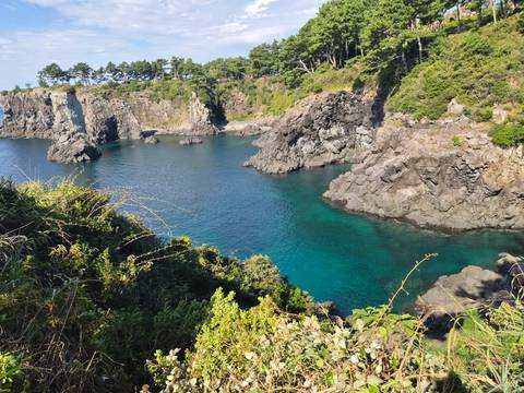 Clear turquoise bay surrounded by dramatic volcanic cliffs and lush greenery.