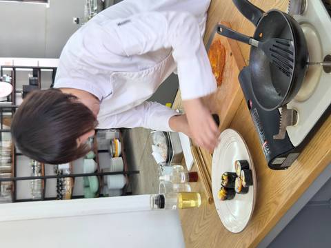 Chef in white prepares kimbap rolls during a hands-on cooking class.