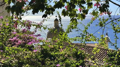 Bougainvillea frames the tiled dome of Positano’s church with sparkling sea beyond.