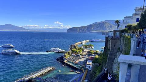 Panoramic view of Sorrento port with ferries, cliffs and Mount Vesuvius in distance.