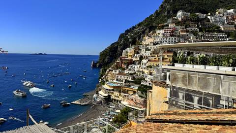 Colorful cliffside houses cascade toward Positano’s dark-sand beach dotted with boats.