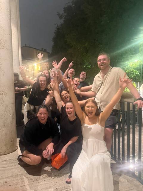 Joyful group of travellers cheering with raised arms during a night out in Rome.