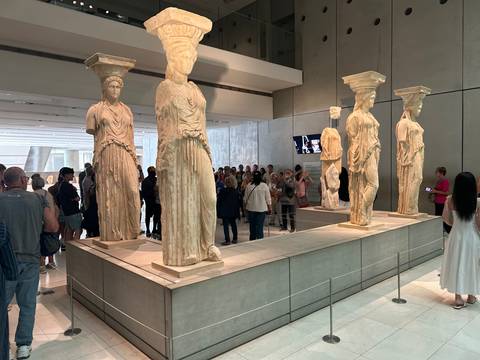 Visitors observe the original Caryatid statues displayed inside the Acropolis Museum.