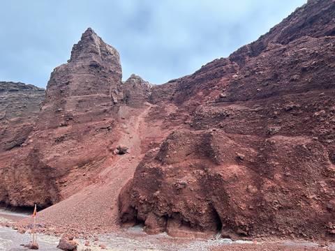 Towering red volcanic cliffs form a rugged canyon beneath a pale blue sky.