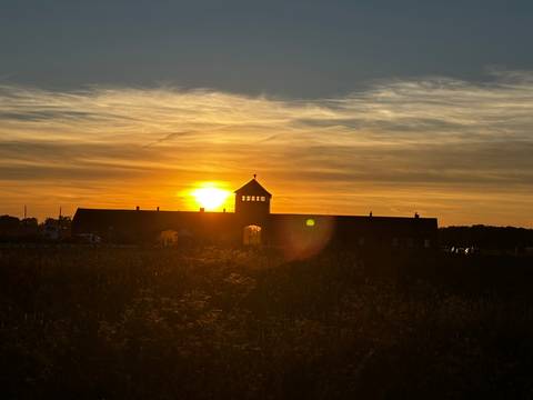 Silhouette of the Auschwitz Birkenau gatehouse against a dramatic orange sunset sky.