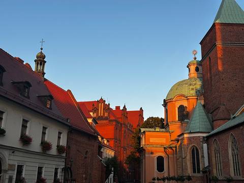 Warm evening light bathes red-brick historic buildings and church domes in a Polish old town street.