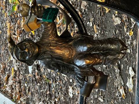 A whimsical bronze gnome sculpture in Wroclaw sits holding padlocks fastened to a railing.