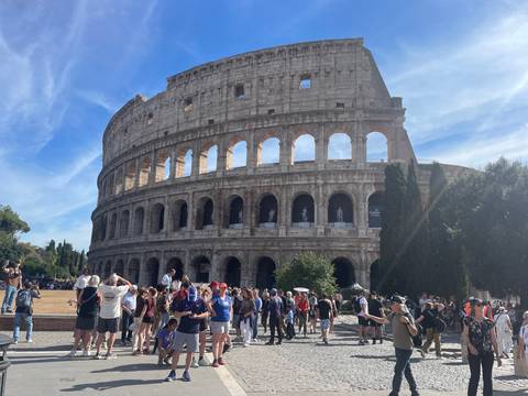 Rome’s Colosseum looms grandly as crowds of tourists explore the ancient amphitheater on a sunny day.