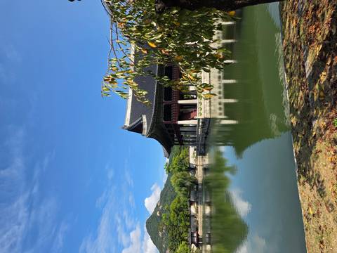 Traditional palace pavilion reflected in a tranquil pond with blue sky backdrop