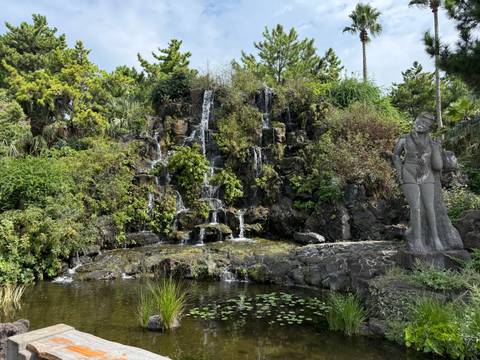 Rocky garden waterfall cascading into a pond surrounded by lush greenery and a statue