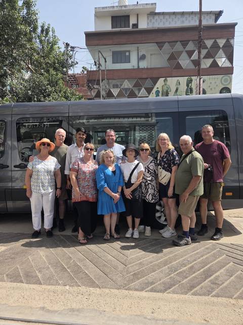 Tour group poses in front of their grey passenger van before departure.