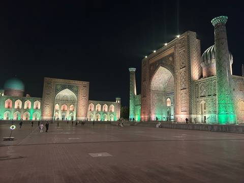 Registan Square’s illuminated madrasas glow green against the night sky in Samarkand.
