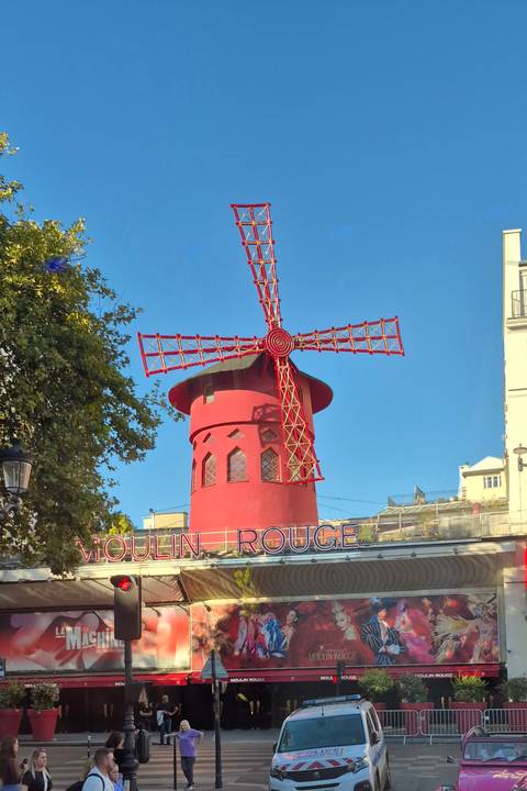 Bright red windmill of the Moulin Rouge stands out against a clear blue Paris sky.