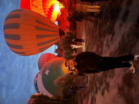 Hot-air balloons inflate pre-dawn in Cappadocia while travellers gather on the field.