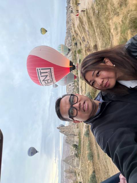Selfie of couple with red balloon and Cappadocia rock formations behind.