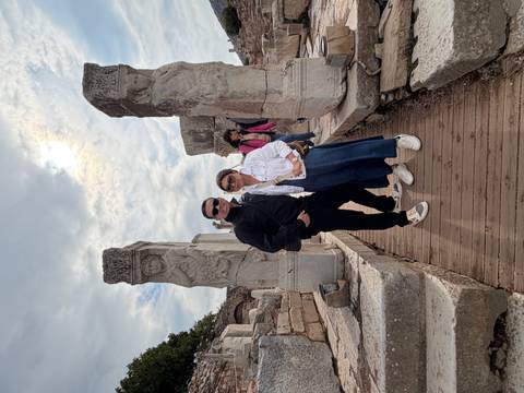 Couple stands among ancient columns in the ruins of Ephesus on a cloudy day.