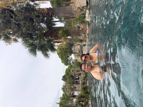 Couple relax in the warm mineral waters of Pamukkale’s thermal pool among palm trees.