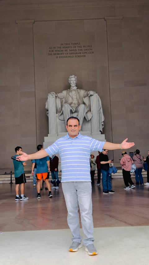 Smiling man with open arms poses in front of the seated Lincoln statue inside the Lincoln Memorial