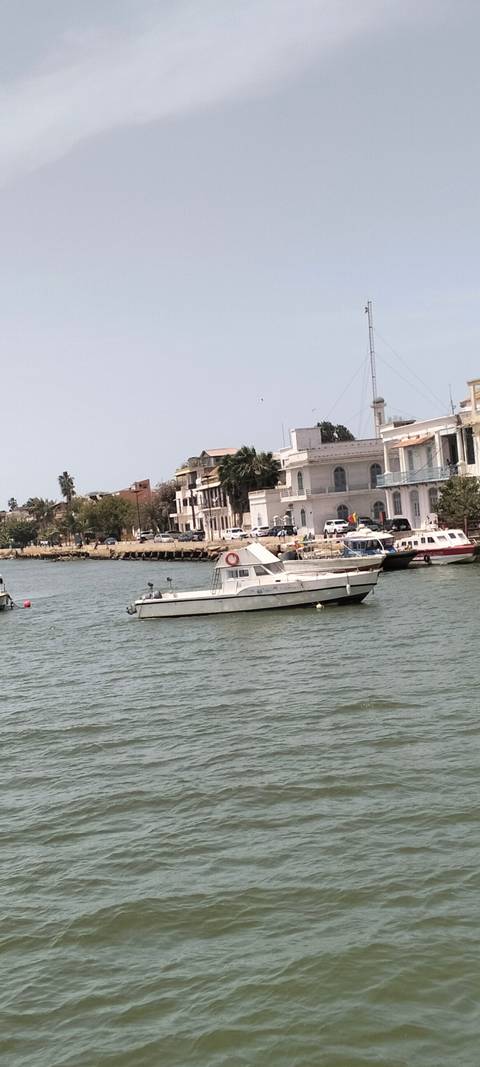 Small leisure boats float on a calm river lined with colonial buildings and palms