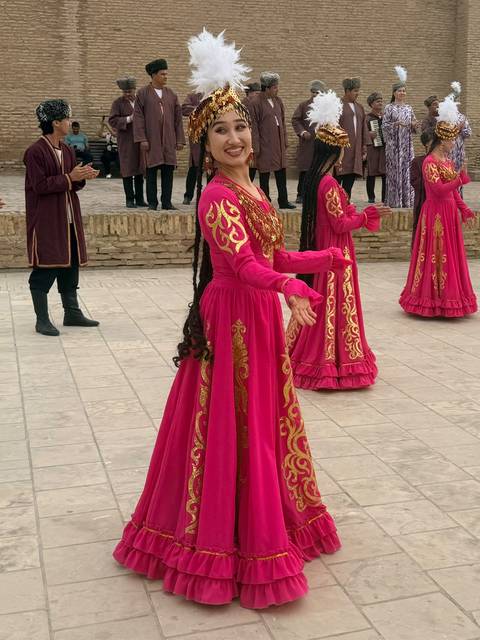 Women in bright pink traditional dresses performing a folk dance in a historic brick courtyard