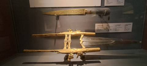 Display case of ornate historical daggers and firearms in a dimly lit museum