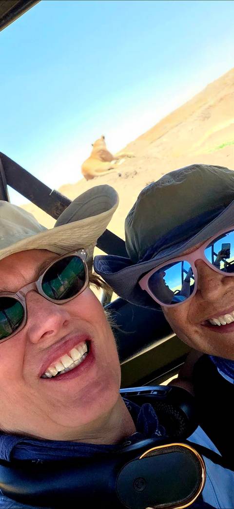 Close-cropped selfie of two travelers wearing hats and sunglasses inside a vehicle.