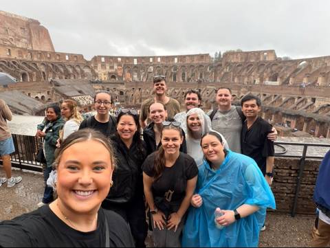 Smiling tour group taking a selfie inside the ancient Colosseum on an overcast day.