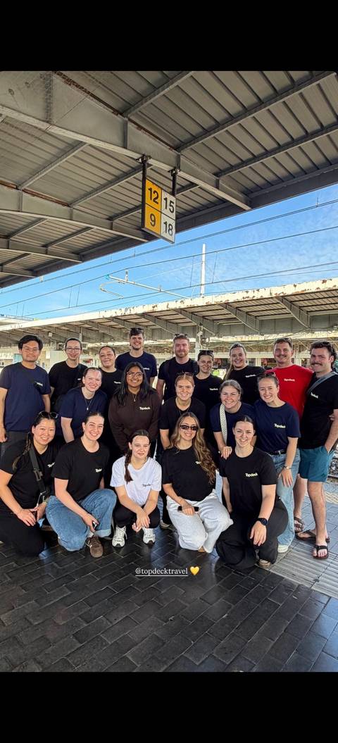 Large travel group in matching shirts gathered for a photo on a railway platform.