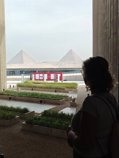 Repeat view of a museum visitor silhouetted against windows looking toward two pyramids.