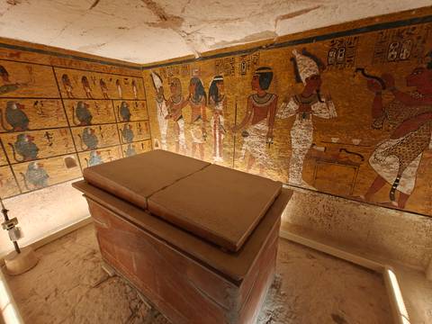 Interior of an Egyptian tomb decorated with colorful hieroglyphic murals and a stone sarcophagus.