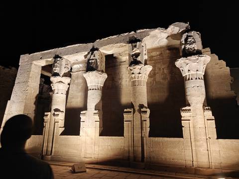 Columns of an ancient Egyptian temple illuminated dramatically at night against a dark sky.