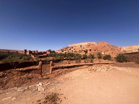 Adobe ksar of Ait Benhaddou rises above palm groves under cloudless desert sky