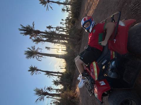 Rider lounging on red quad bike with helmet among tall palm trees at sunset near Marrakesh.