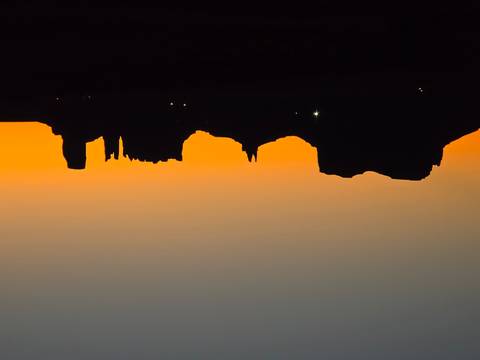 Silhouetted mesas of Monument Valley stand against a vivid orange sunrise horizon.