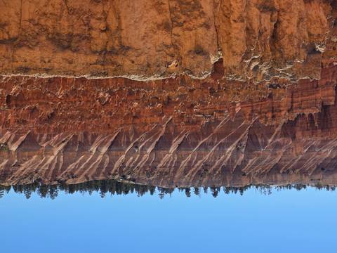 Steep red hoodoos and striped cliffs fill the amphitheatre of Bryce Canyon under a clear sky.