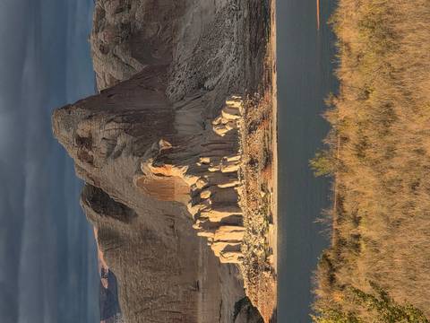 Sunlit rock formations rise from Lake Powell’s shoreline beneath brooding storm clouds.