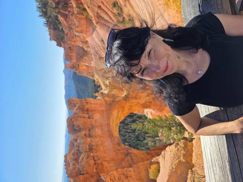 A woman smiles at a viewpoint overlooking Bryce Canyon’s Natural Bridge arch.