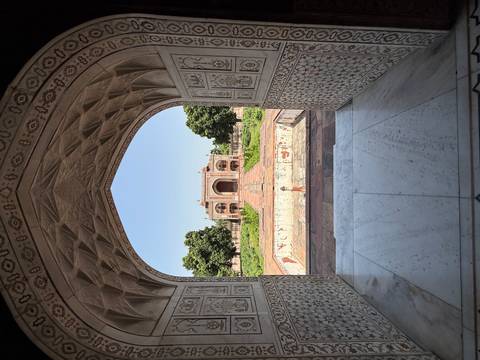 View through a marble archway toward the ornate gateway of Humayun's Tomb, India.