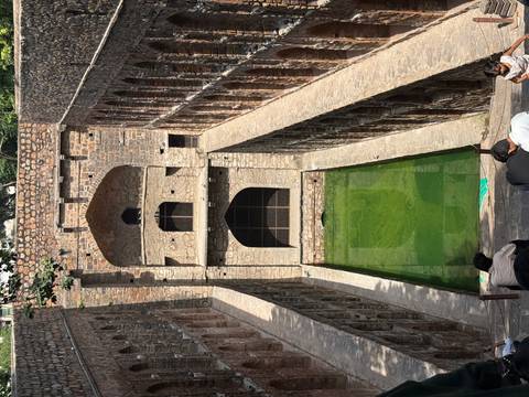 Deep stone stepwell with green water at the bottom and arched corridors rising on each side.