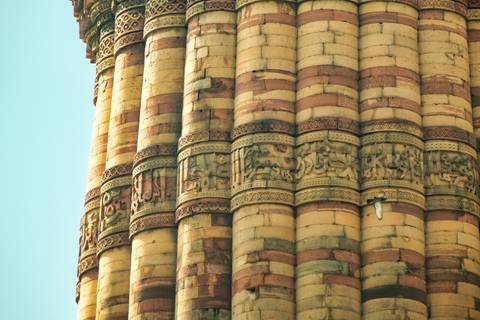 Stone shafts of Qutub Minar with intricate carvings and alternating sandstone bands in warm sunlight.