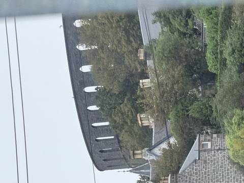 Distant stone circular tower ruins atop a hill partially obscured by trees and rooftops on a gloomy day.